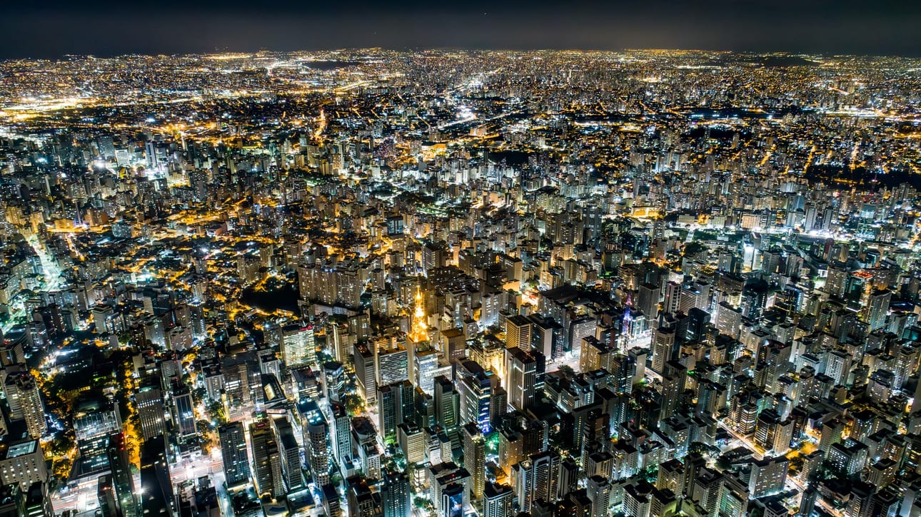 Bacurau Noturno 2, fotografia fine art de Bruno Boni. Vista aérea de São Paulo à noite, com a malha de avenidas iluminadas correndo em direção a um horizonte que não…