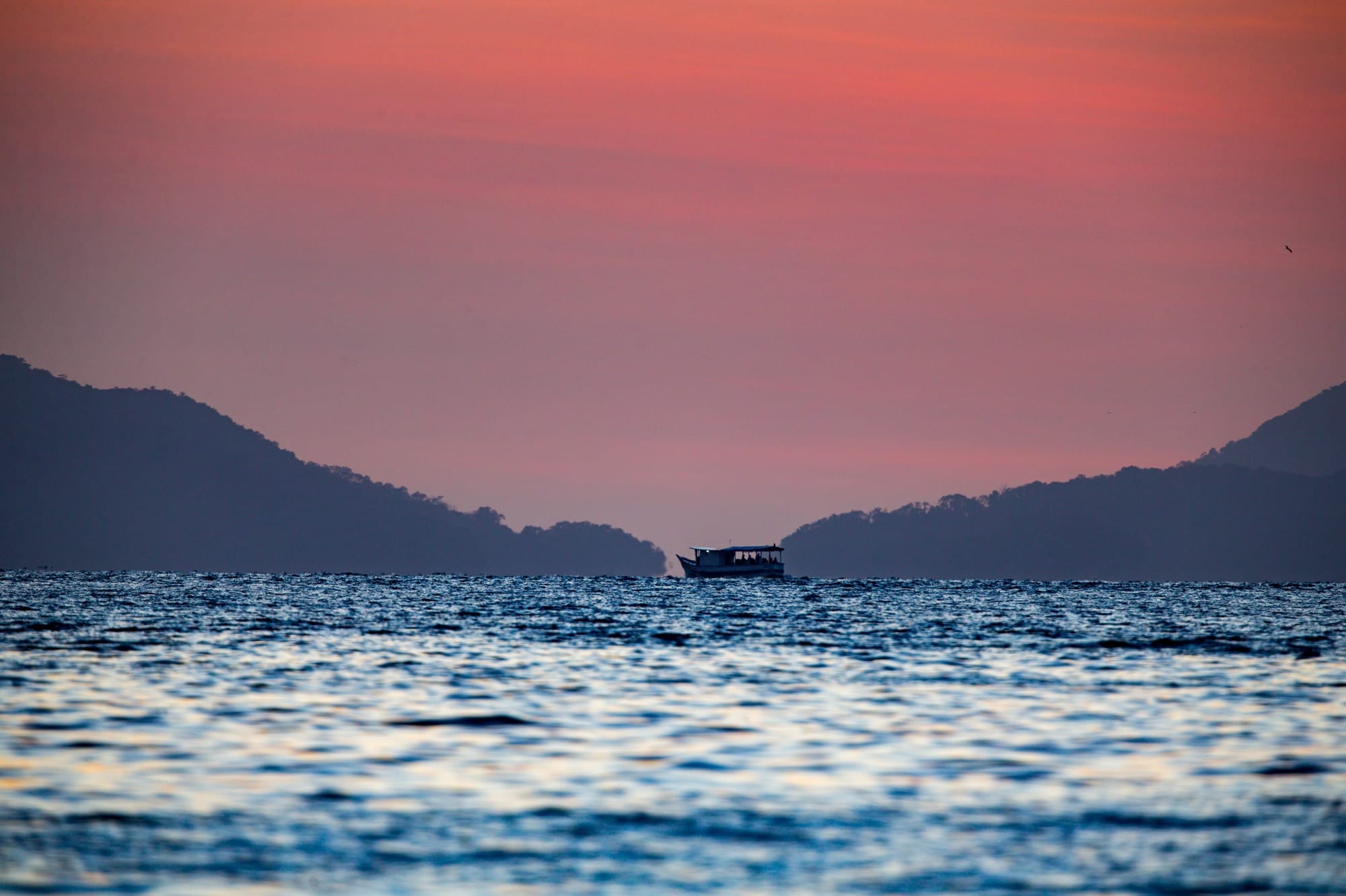 Little Boat in the Lagoa Azul Channel, fine art photograph by Bruno Boni. A small boat crosses slowly in front of the Lagoa Azul channel, on Ilha Grande, just before sunrise. The sea ripples in…