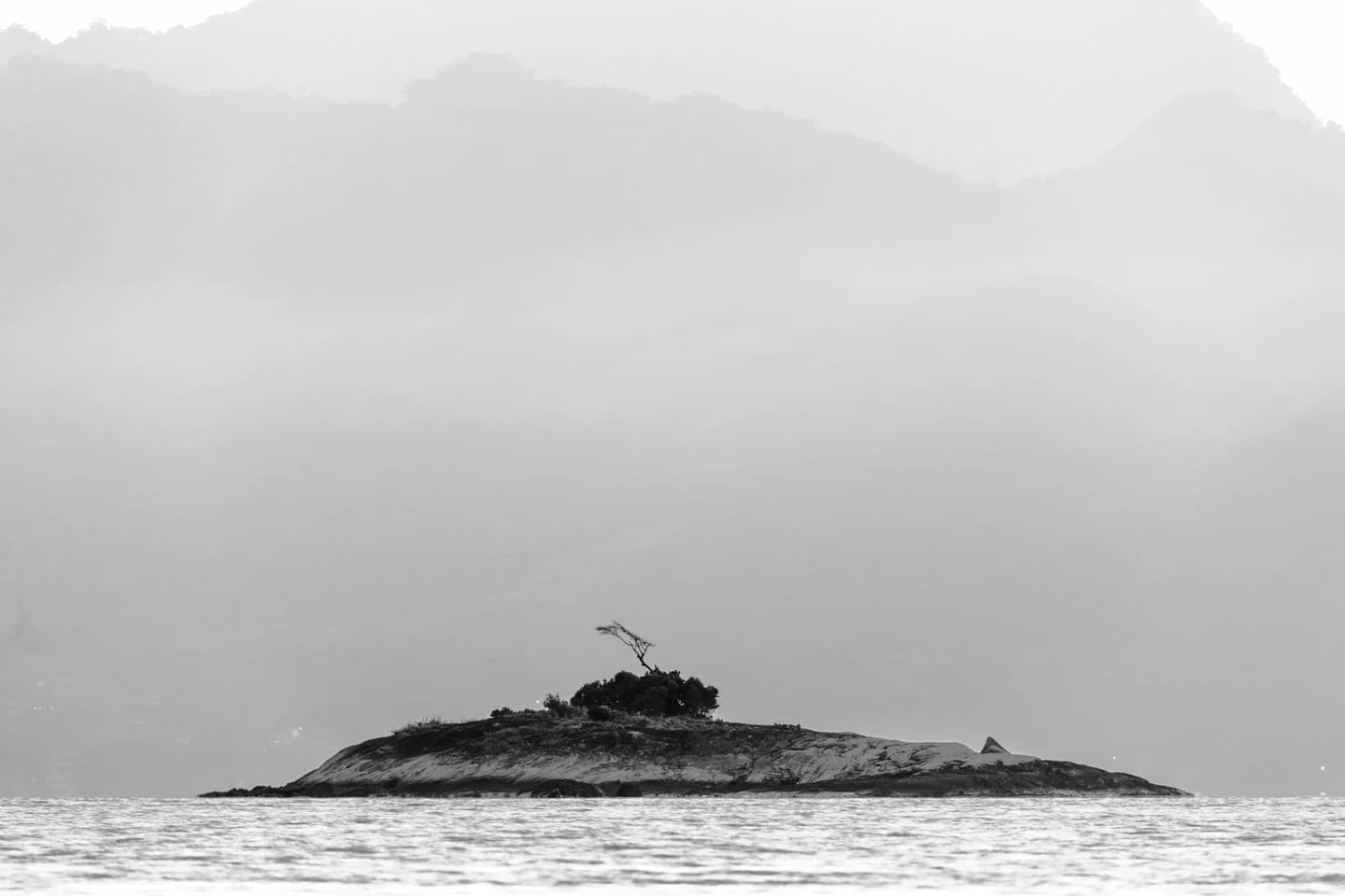 Botinas P&B, fotografia fine art de Bruno Boni. As pequenas Ilhas das Botinas surgem como silhueta diante da presença imponente da Ilha Grande ao fundo, reforçando o…