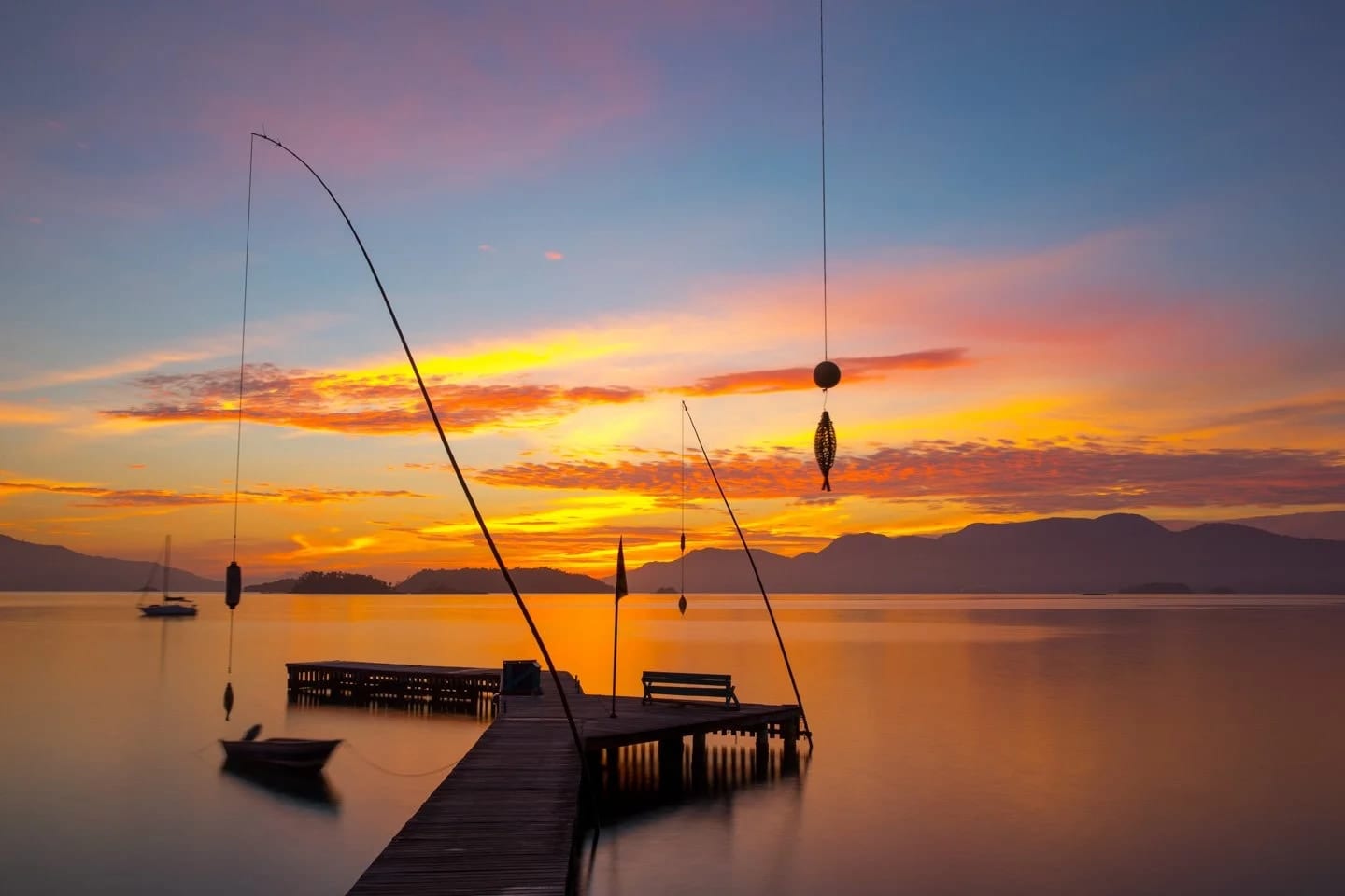 Cais do Seu Luiz, fotografia fine art de Bruno Boni. O cais de madeira do tradicional Bar do Luiz, em Angra dos Reis, avança sobre a água calma ao amanhecer, iluminado…