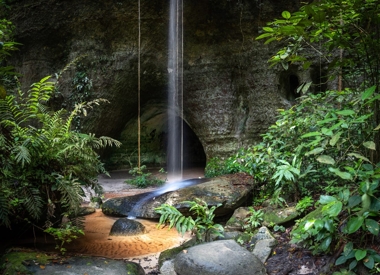 Caverna do Maroaga 1, fotografia fine art de Bruno Boni. Na entrada da Caverna do Maroaga, em Presidente Figueiredo, um véu de água despenca da borda de pedra e encontra o…