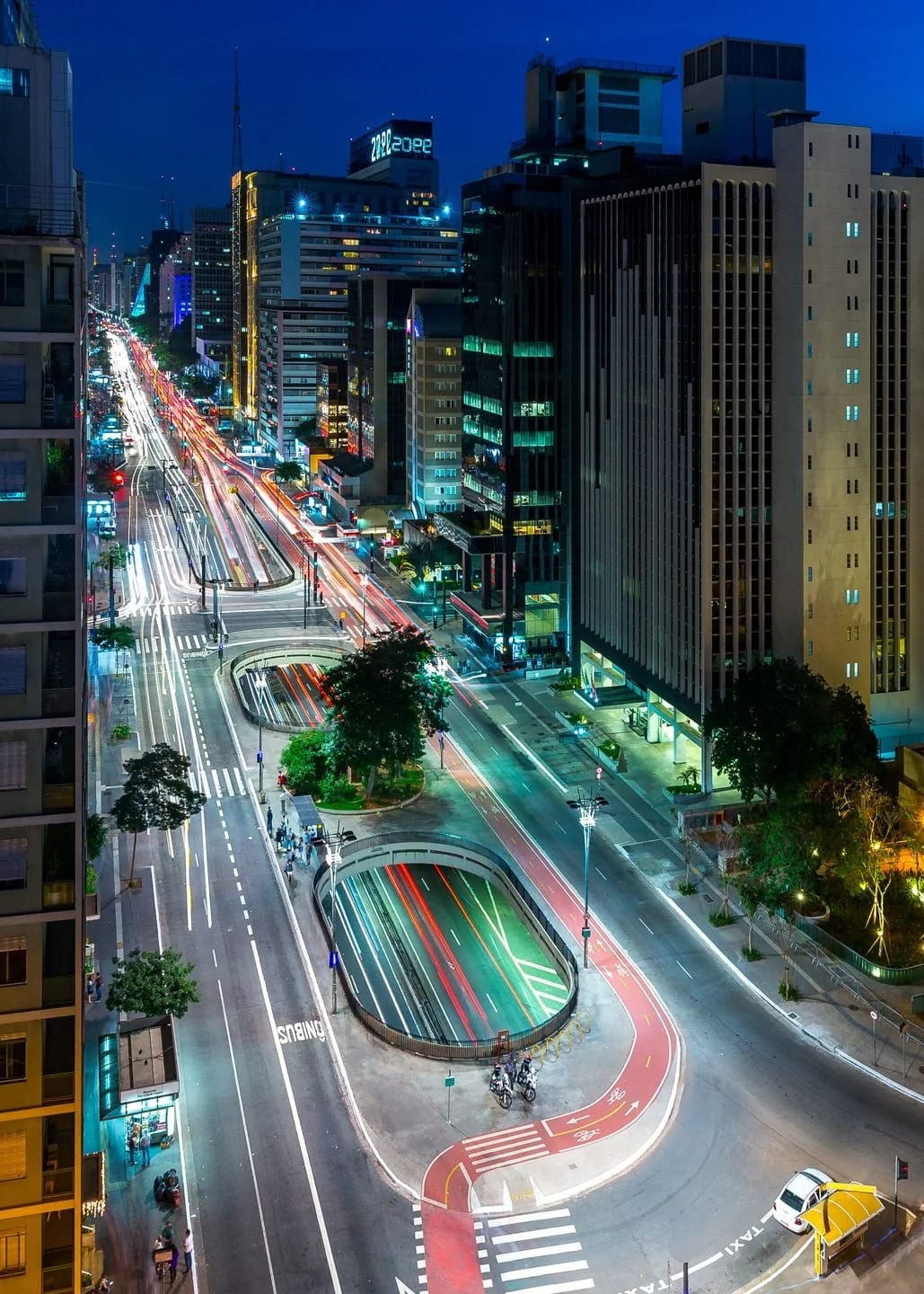 Paulista Circuit, fine art photograph by Bruno Boni. Paulista Avenue in full blue hour. The oval openings in the central median break the rigidity of the avenue and give…