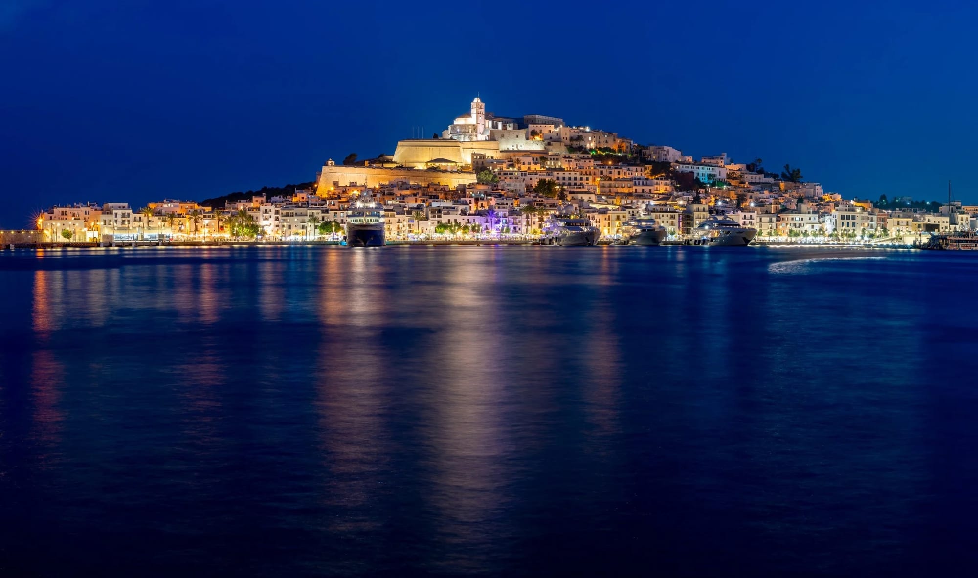 Dalt Vila e Iates, Entre o Medieval e o Moderno, fotografia fine art de Bruno Boni. Panorama noturno de altíssima resolução capturado com técnica de longa exposição, revelando o charme iluminado de Dalt…