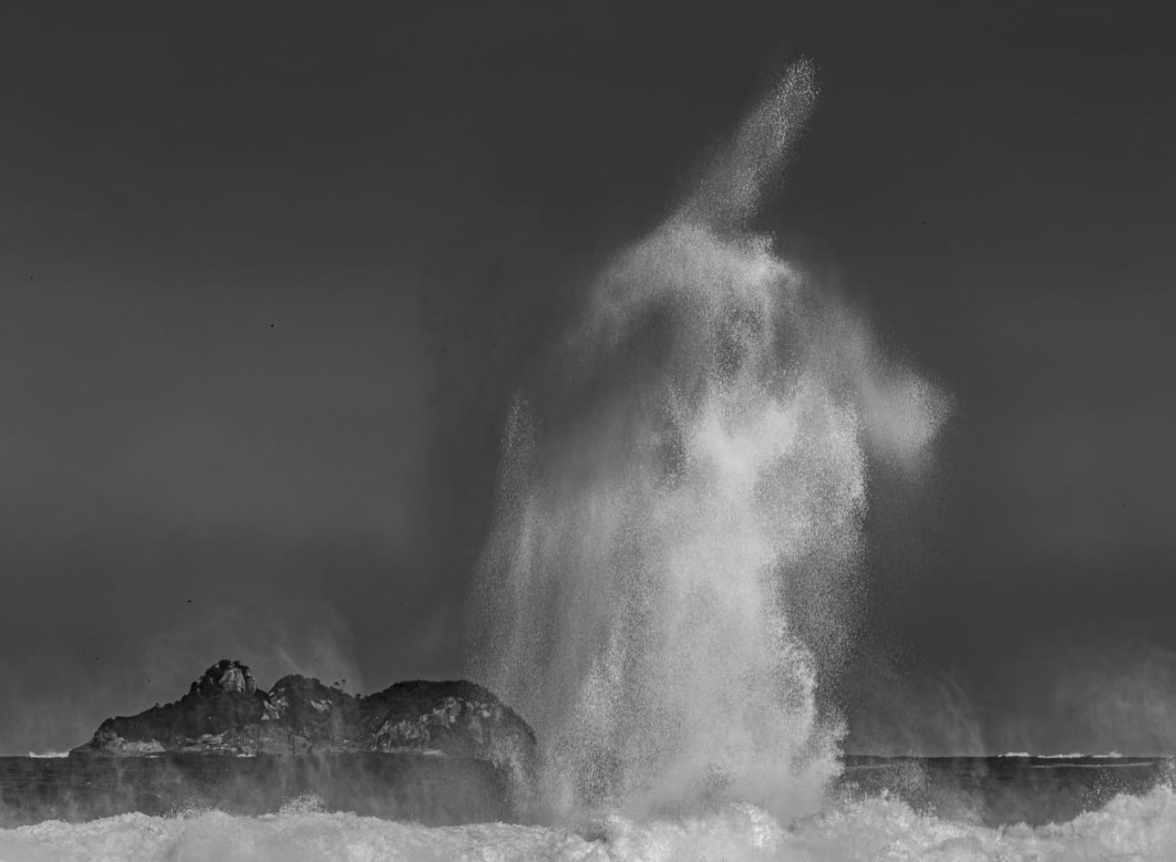 Encontro Explosivo 10, fotografia fine art de Bruno Boni. Depois do impacto contra as pedras de São Conrado, a água pulverizada sobe em uma figura quase fantasmagórica, suspensa…