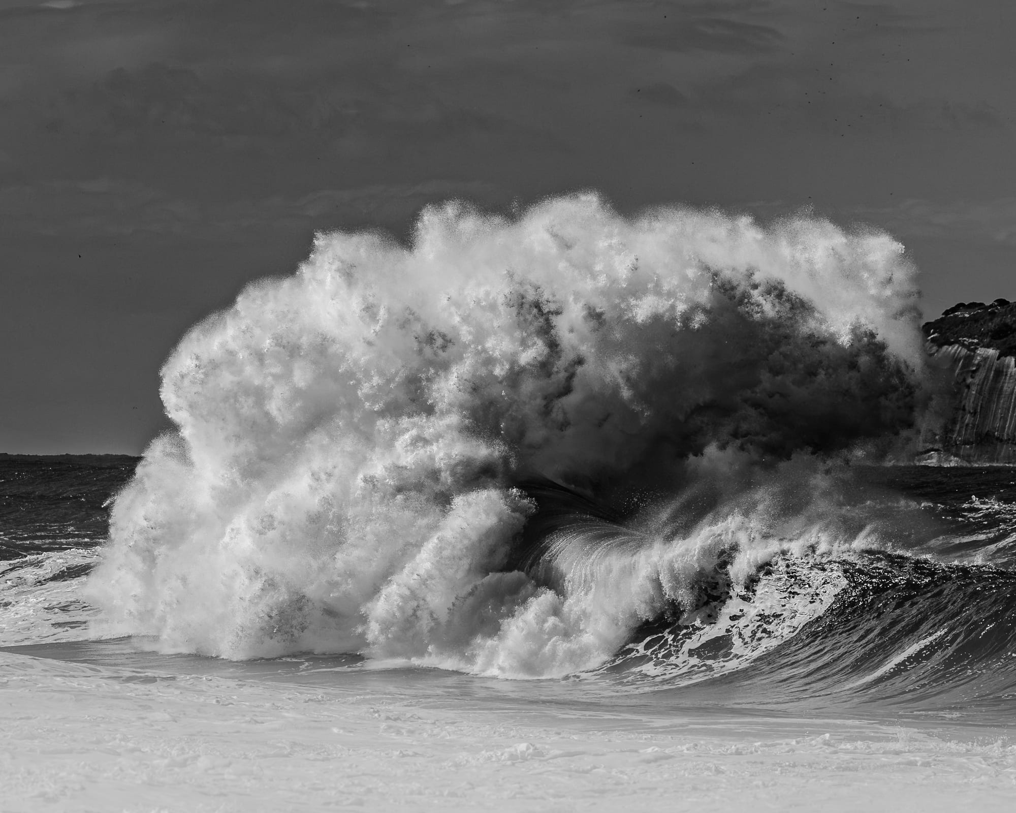 Encontro Explosivo 2, fotografia fine art de Bruno Boni. A massa de espuma toma quase todo o quadro, densa como uma nuvem de tempestade pousada sobre o mar de São Conrado, no…