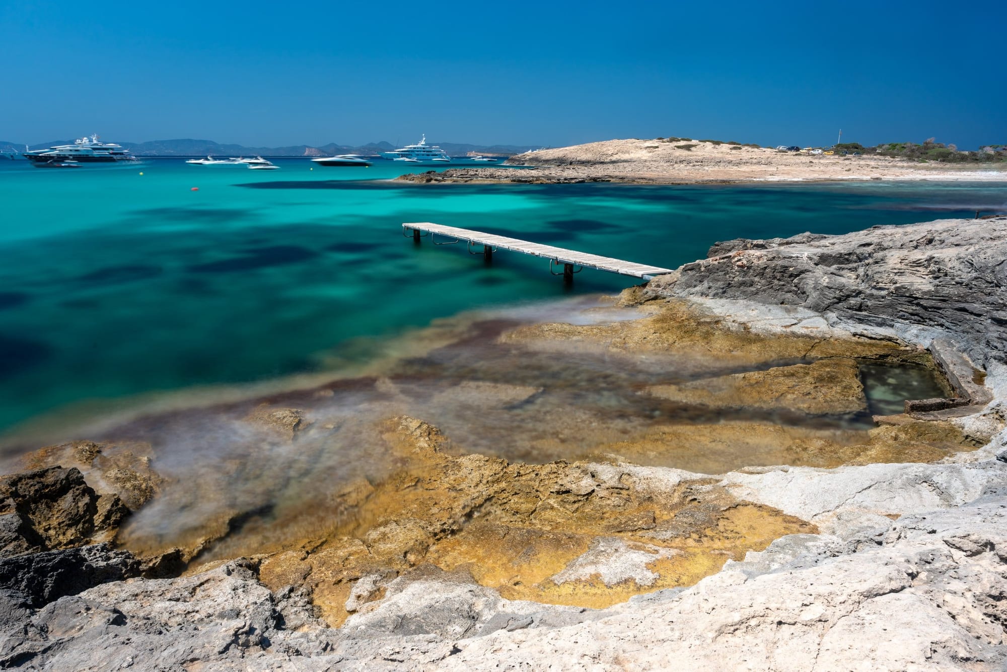 Azul de Es Molí, fotografia fine art de Bruno Boni. Do costão de Es Molí de Sal, em Formentera, a rocha dourada avança em lajes sobre a água transparente, guardando uma…