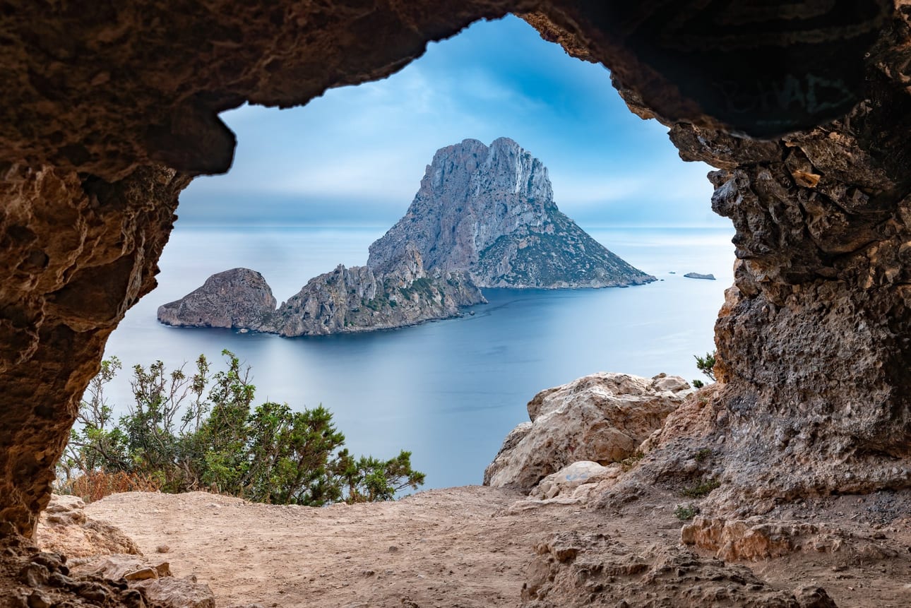 Es Vedrà Portal, fine art photograph by Bruno Boni. Framed by the rocky portal of a cave, the mythical islet of Es Vedrà rises over the silken Mediterranean, the result of…