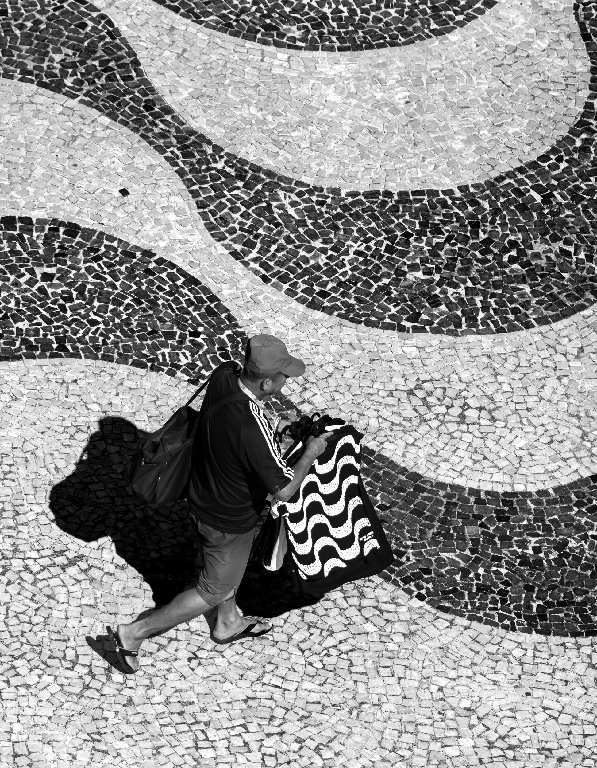 Meta Ondas, fotografia fine art de Bruno Boni. Ondas sobre ondas: a orla de São Conrado vira um mar de pedra, e nele caminha um único homem, vendendo camisetas que…