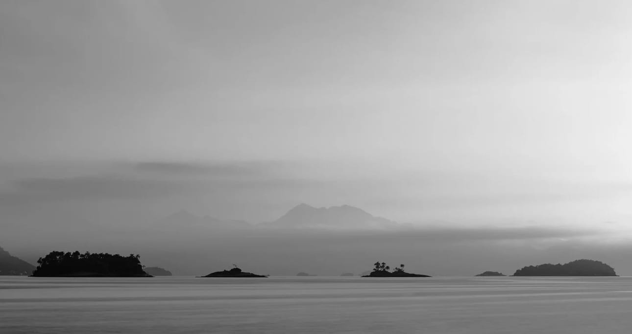 Primeira Luz em Angra P&B, fotografia fine art de Bruno Boni. Manhã em Angra sob camadas de névoa e luz, aqui traduzida em preto e branco. Sem a cor, a cena se reduz ao essencial…