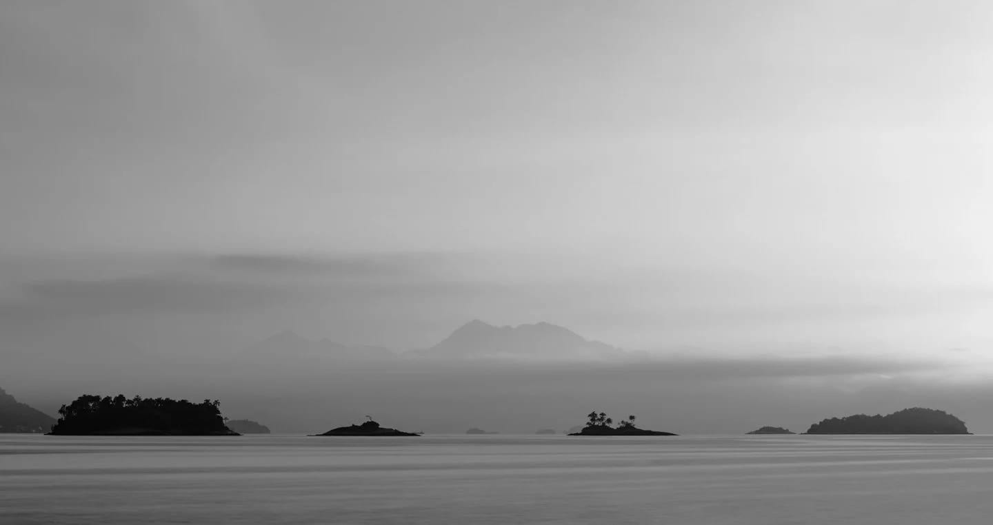 First Light in Angra B&W, fine art photograph by Bruno Boni. Morning in Angra beneath layers of mist and light, here rendered in black and white. Without color, the scene is…