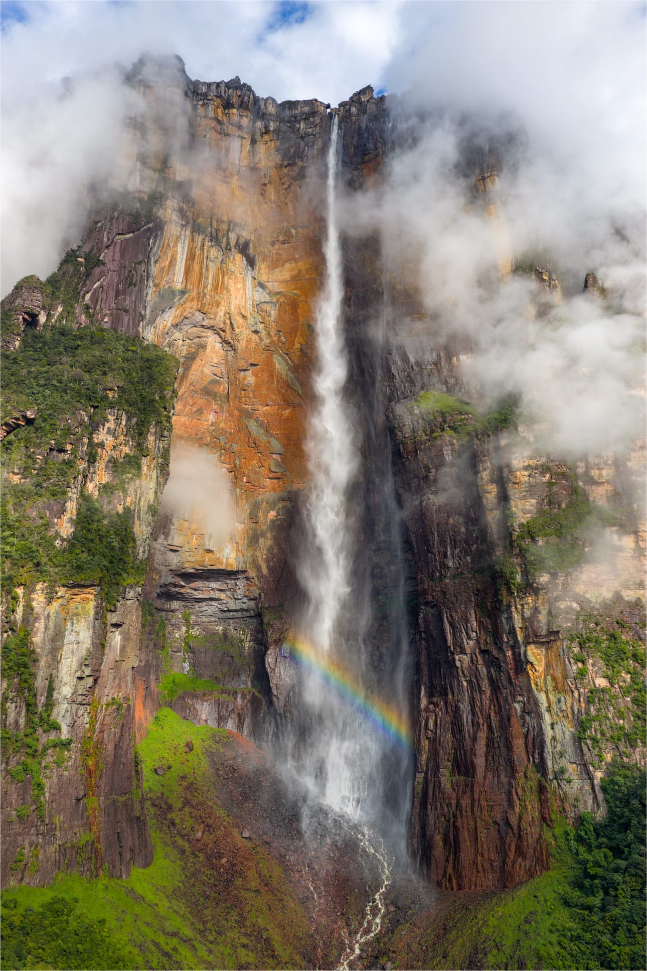 Salto Angel 2, fotografia fine art de Bruno Boni. O paredão do Salto Angel de frente, com a rocha em tons de ocre e as nuvens envolvendo o topo do tepui. A água cai em…